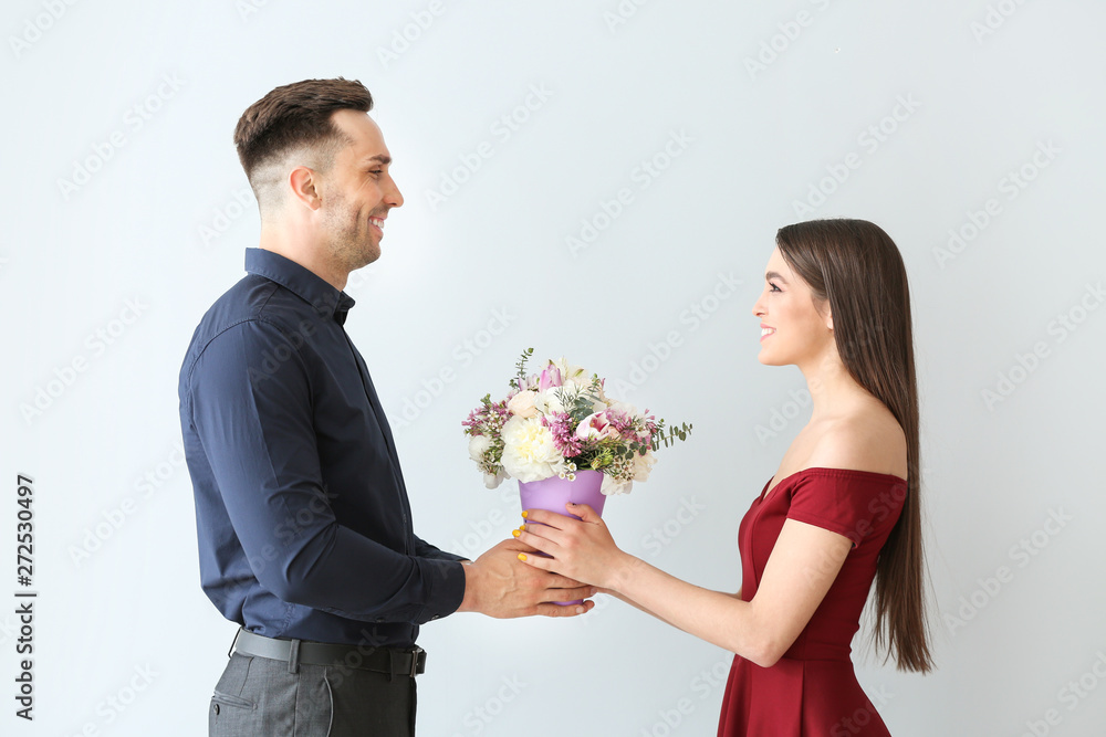 Woman receiving flowers from young man on light background Woman receiving flowers from young man on light background