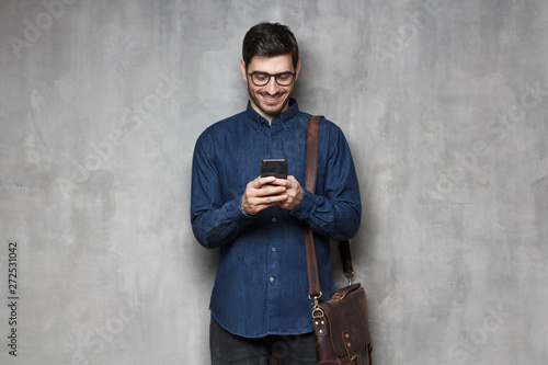 European male isolated on gray background exchanging messages via cellphone and smiling