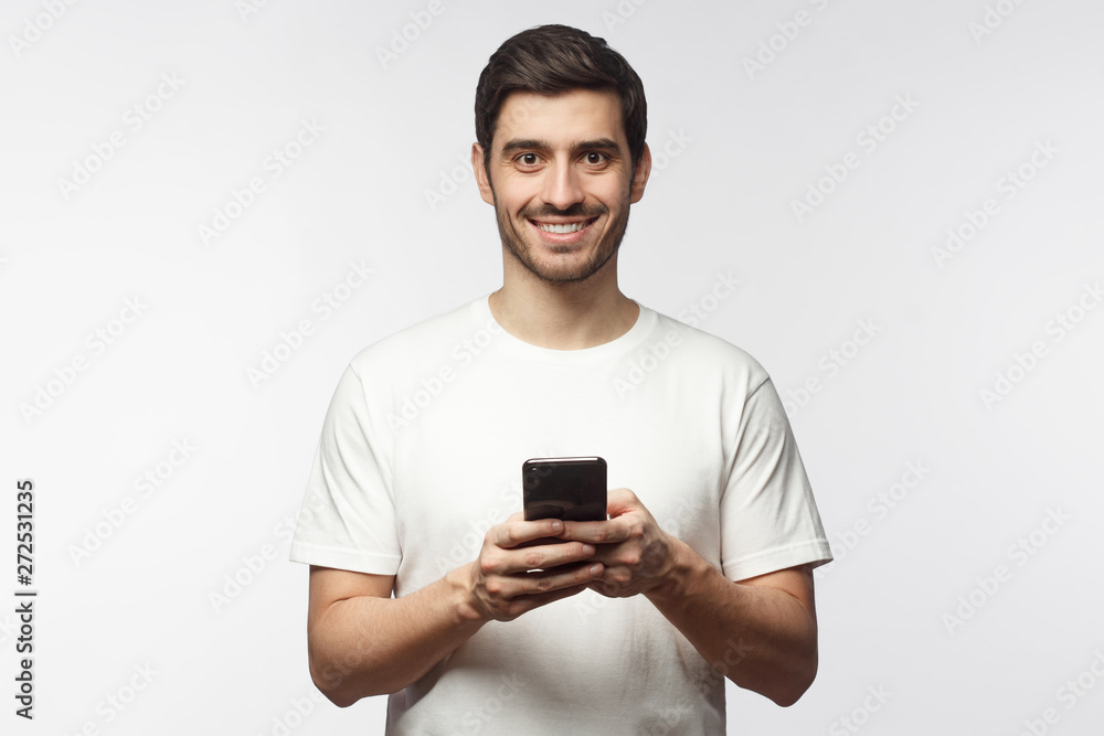 European Caucasian guy standing with smartphone in hands against light gray background European Caucasian guy standing with smartphone in hands against light gray background