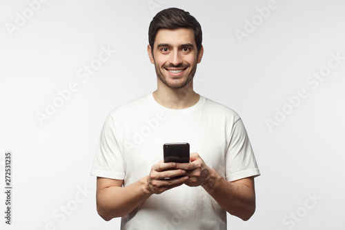 European Caucasian guy standing with smartphone in hands against light gray background © Damir Khabirov