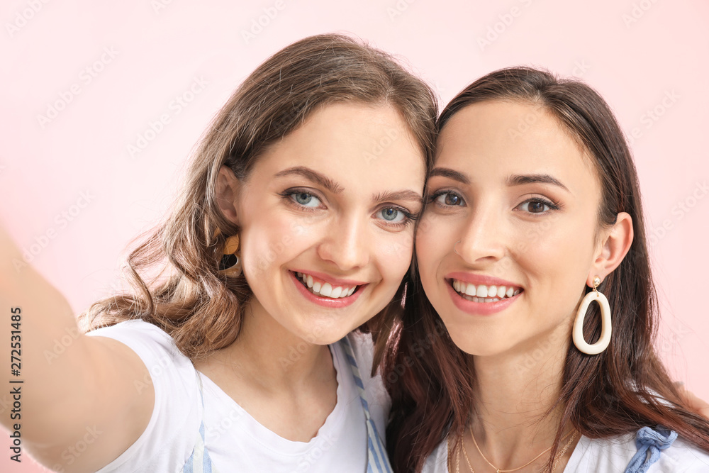 Portrait of happy lesbian couple taking selfie on color background Portrait of happy lesbian couple taking selfie on color background