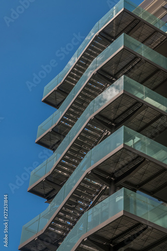 Business building with metal emergency ladder / fire escape in modern office buildings with repeating structure and reflected sky and clouds.