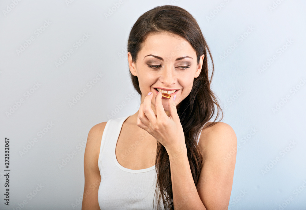 Happy smiling positive woman eating the pill and holding the glass of water in the hand on blue background. Closeup Happy smiling positive woman eating the pill and holding the glass of water in the hand on blue background. Closeup