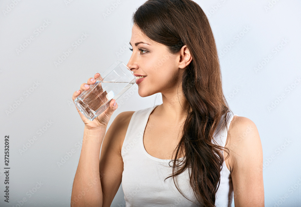 Positive happy smiling woman with healthy skin and long curly hair drinking pure water on blue background. Closeup Positive happy smiling woman with healthy skin and long curly hair drinking pure water on blue background. Closeup
