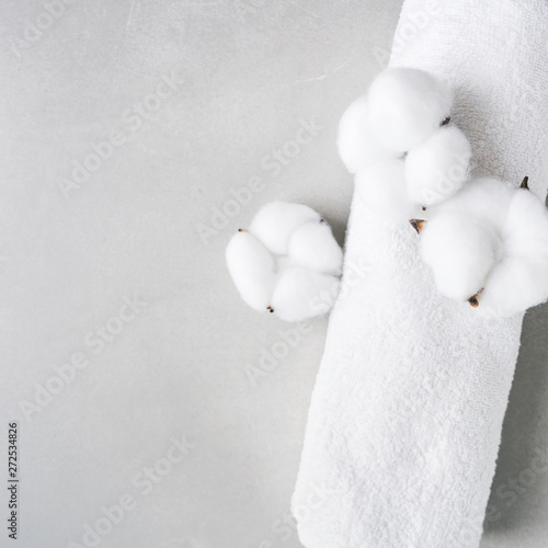 White fluffy towel twisted into roll with flowers of natural cotton on gray background with copy space. Spa concept. Flat lay. © PINKASEVICH