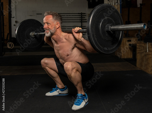Ein durchtrainierter Mann mittleren Alters macht oberkörperfrei Squats. Fitnesstraining mit der Langhantel. Training mit Gewichten.