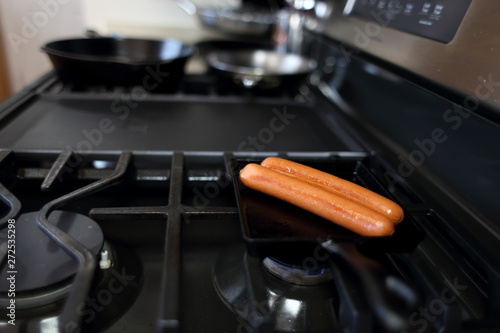 Hotdogs cooking on a raclette pan on a natural gas stove.