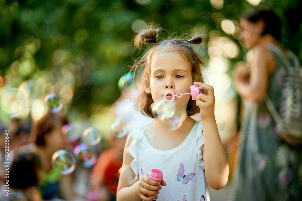 Little cute baby girl is making soap bubbles in the park on summer day