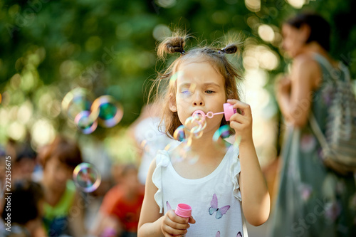 Little cute baby girl is making soap bubbles in the park on summer day