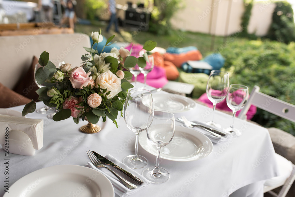 Wedding table setting decorated with fresh flowers in a brass vase. Wedding floristry. Banquet table for guests outdoors with a view of green nature. Bouquet with roses, eustoma and eucalyptus leaves Wedding table setting decorated with fresh flowers in a brass vase. Wedding floristry. Banquet table for guests outdoors with a view of green nature. Bouquet with roses, eustoma and eucalyptus leaves