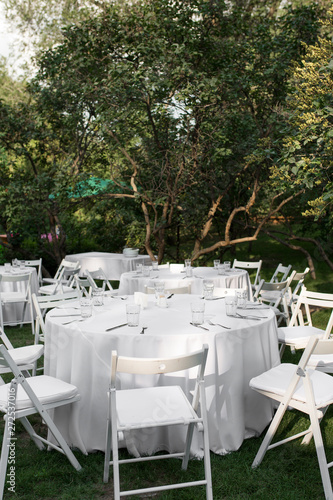 Wedding table setting decorated with fresh flowers in a brass vase. Wedding floristry. Banquet table for guests outdoors with a view of green nature. Bouquet with roses, eustoma and eucalyptus leaves