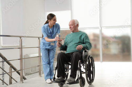 Nurse giving water to senior man in wheelchair at hospital. Medical assisting