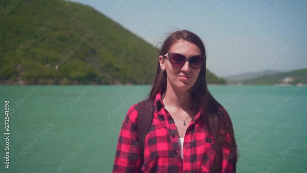Portrait of a young attractive girl in a red checkered shirt, posing in front of the camera. On a warm day, a girl stands on the shore of a lake, with a white swan in the background. Portrait of a young attractive girl in a red checkered shirt, posing in front of the camera. On a warm day, a girl stands on the shore of a lake, with a white swan in the background.