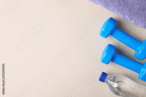 Vinyl dumbbells, towel and bottle of water on color background, flat lay. Space for text