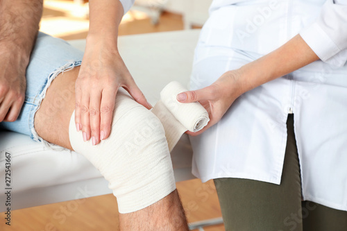 Valokuva Doctor applying bandage to patient's knee in clinic, closeup