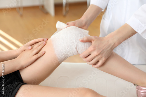 Doctor applying medical bandage to little patient's injured knee in clinic, closeup