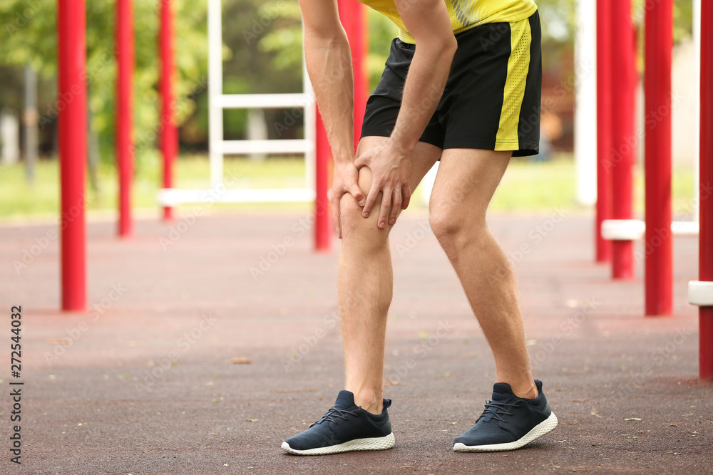 Young man suffering from knee pain on sports ground, closeup Young man suffering from knee pain on sports ground, closeup