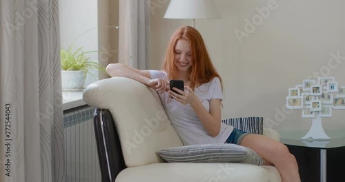 attractive girl sitting at home on the couch using smartphone. in slow motion. Shot on Canon 1DX mark2 4K camera photo