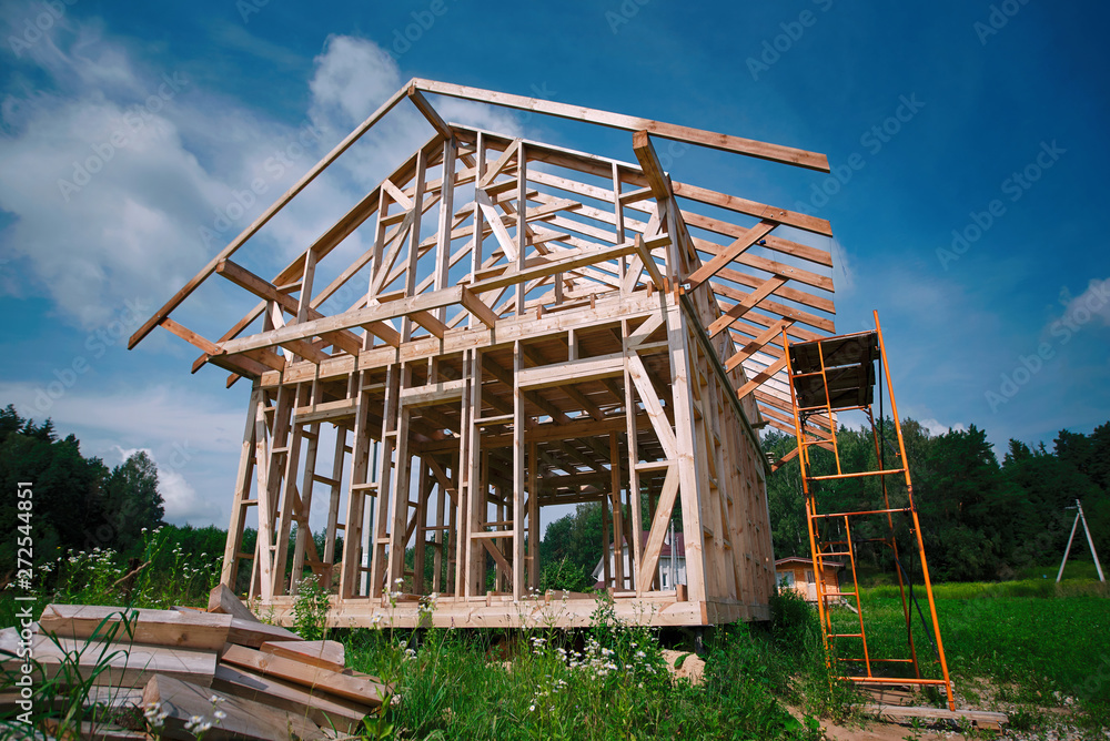 Obraz premium The erection of a wooden frame house. Modern wooden-frame country house under construction. Construction of the roof of a residential house. Unfinished house at construction site.