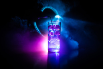 Cocktail glass splashing on dark toned smoky background or colorful cocktail in glass. Party club entertainment. Mixed light.