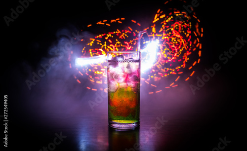 Cocktail glass splashing on dark toned smoky background or colorful cocktail in glass. Party club entertainment. Mixed light.