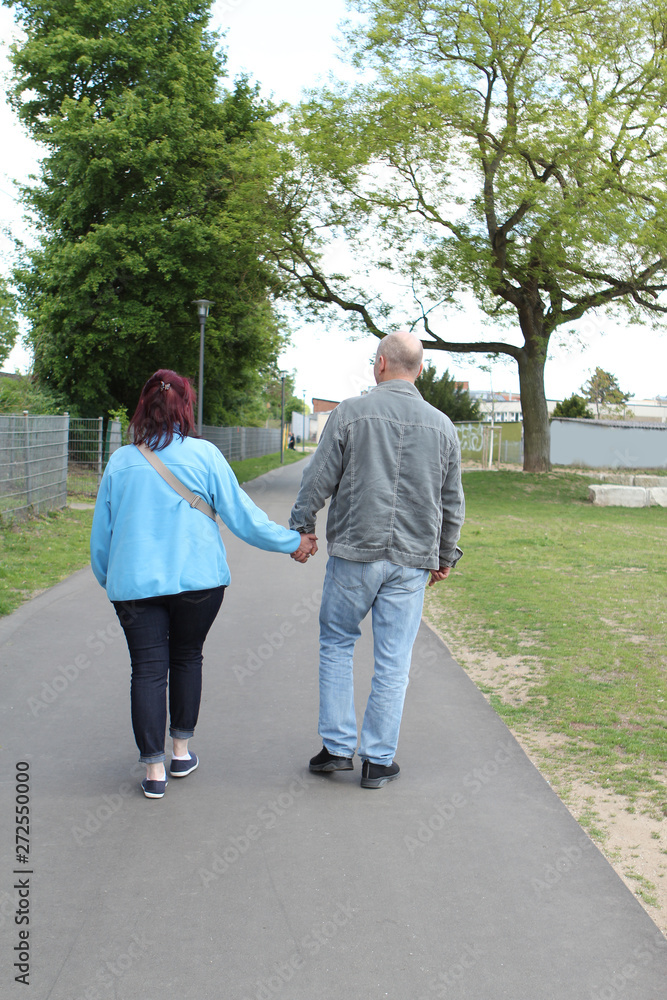 middle aged couple walking down the street holding hands, overweight woman, rear view