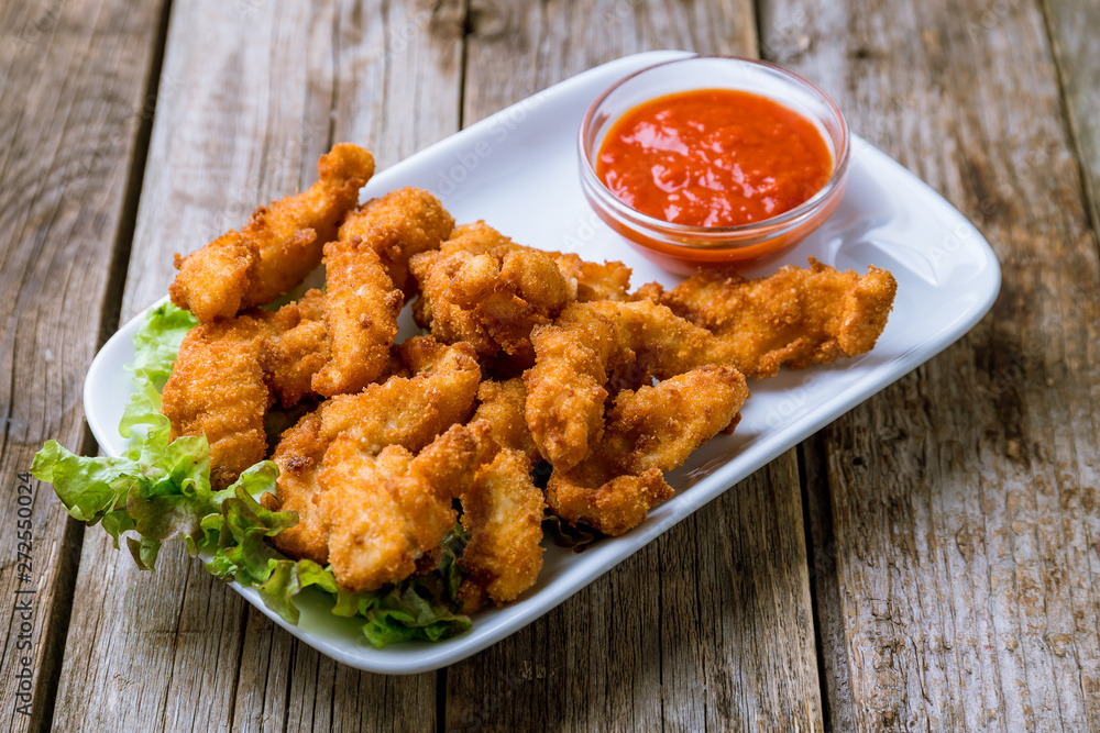 Chicken strips with ketchup on white plate on wooden background Chicken strips with ketchup on white plate on wooden background