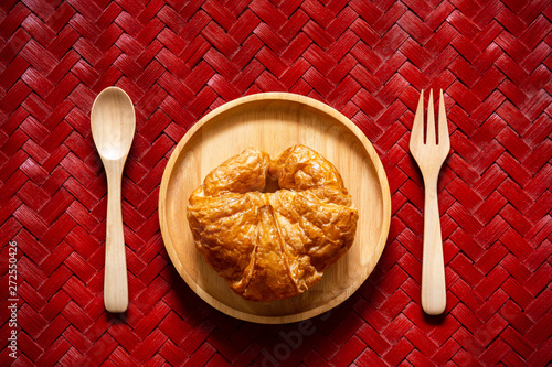 Top view croissants on wooden dish with spoon and fork on texture of woven bamboo.