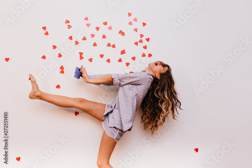 Slim barefooted lady in sleepwear having fun during morning tea. Carefree white girl fooling around while posing with cup of coffee. photo