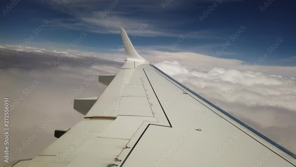 Airliner wing entering a thick layer of clouds under a blue sky with sun Airliner wing entering a thick layer of clouds under a blue sky with sun