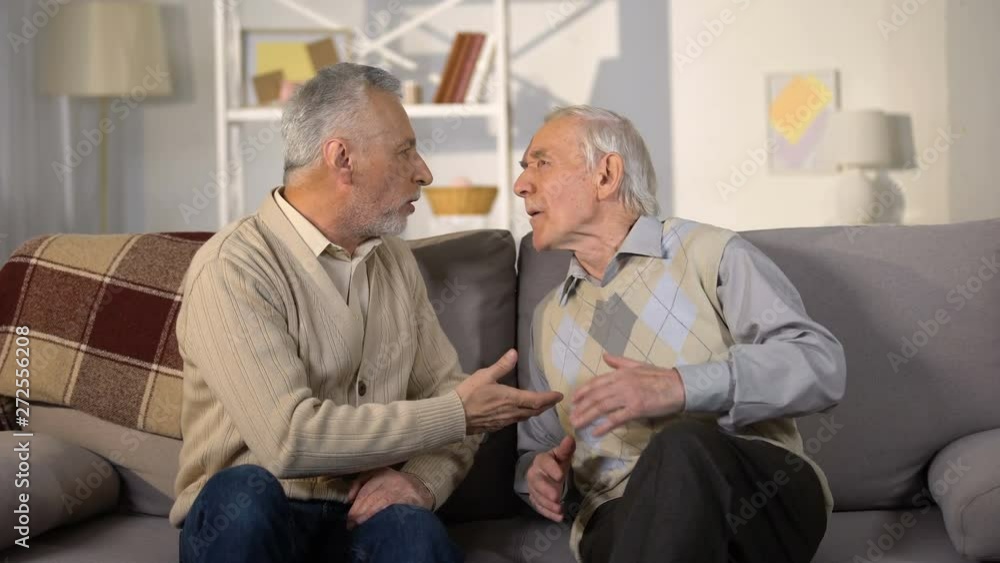 Aged male friends quarrelling on sofa at home, misunderstanding, conflict Aged male friends quarrelling on sofa at home, misunderstanding, conflict