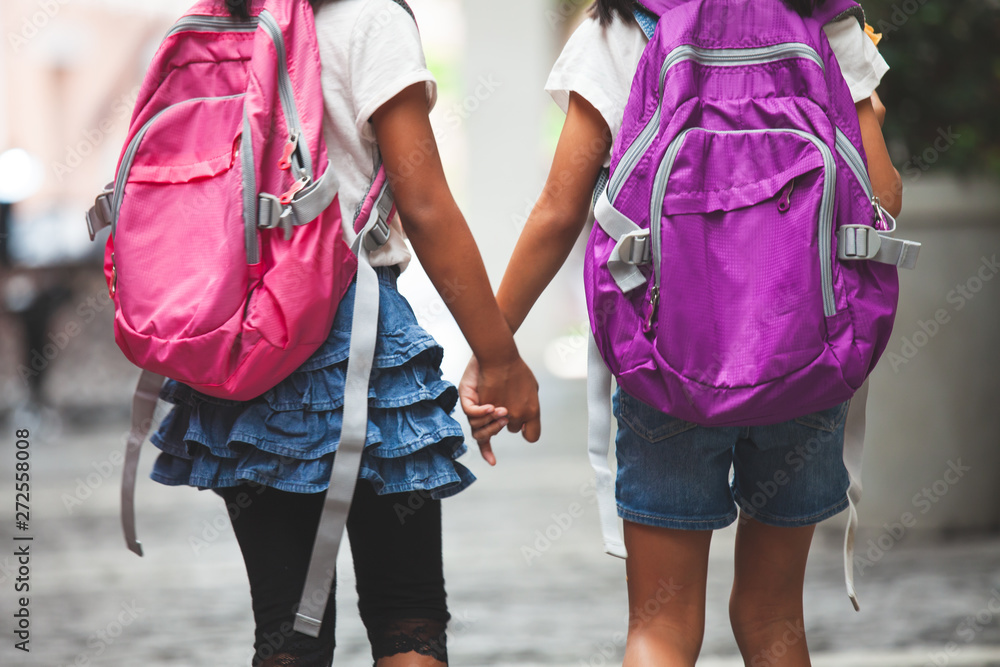 Back to school. Two cute asian child girls with school bag holding hand and walk together in the school - obrazy, fototapety, plakaty 