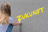 Eine junge Frau schreibt das Wort Zukunft mit der Kreide auf die Straße