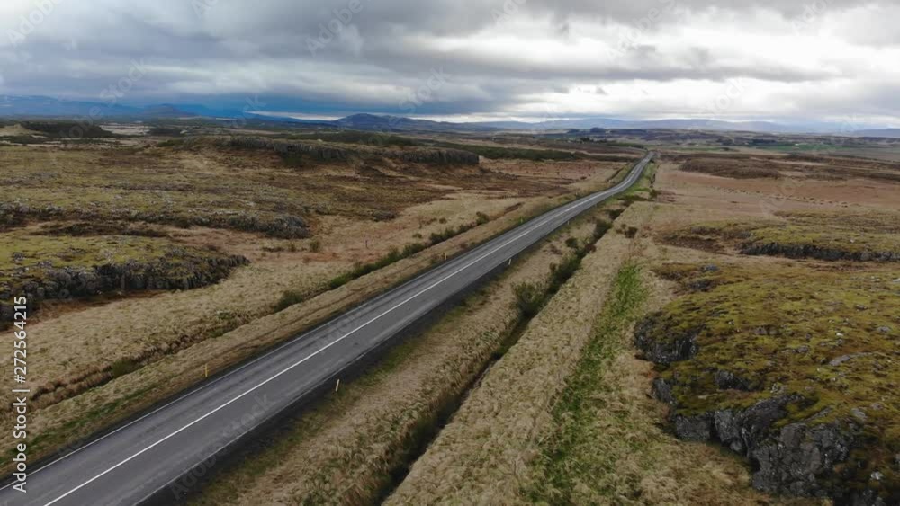 Aerial view of a road leading to an amazing location in the lush green landscape in Iceland with an epic cloudy sky in the background, over big mountains in the distance Aerial view of a road leading to an amazing location in the lush green landscape in Iceland with an epic cloudy sky in the background, over big mountains in the distance