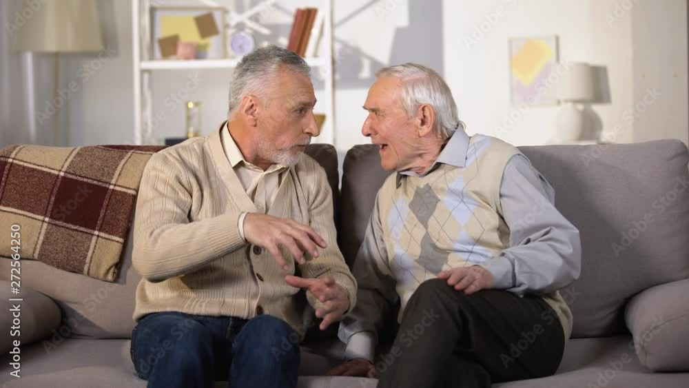 Old man explaining something to deaf friend, sitting on sofa at home, problems Old man explaining something to deaf friend, sitting on sofa at home, problems