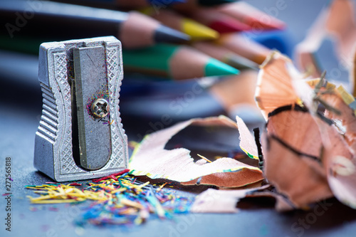 Close up of old and rusty metallic pencil sharpener and color pencil stack with shavings. Dark surface white background