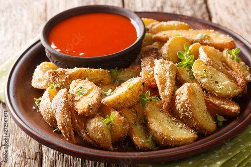 Hot potato wedges with parmesan cheese and oregano with pepper sauce close-up on a plate. horizontal