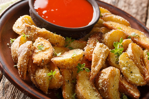 Baked potato wedges with parmesan and oregano, served with pepper sauce close-up on a plate on the table. horizontal