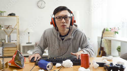 Man addicted to computer games. concentrated young asian male in headset sitting in dirty apartment having fun on internet using keyboard staring pc screen monitor. technology cause eyes near sight