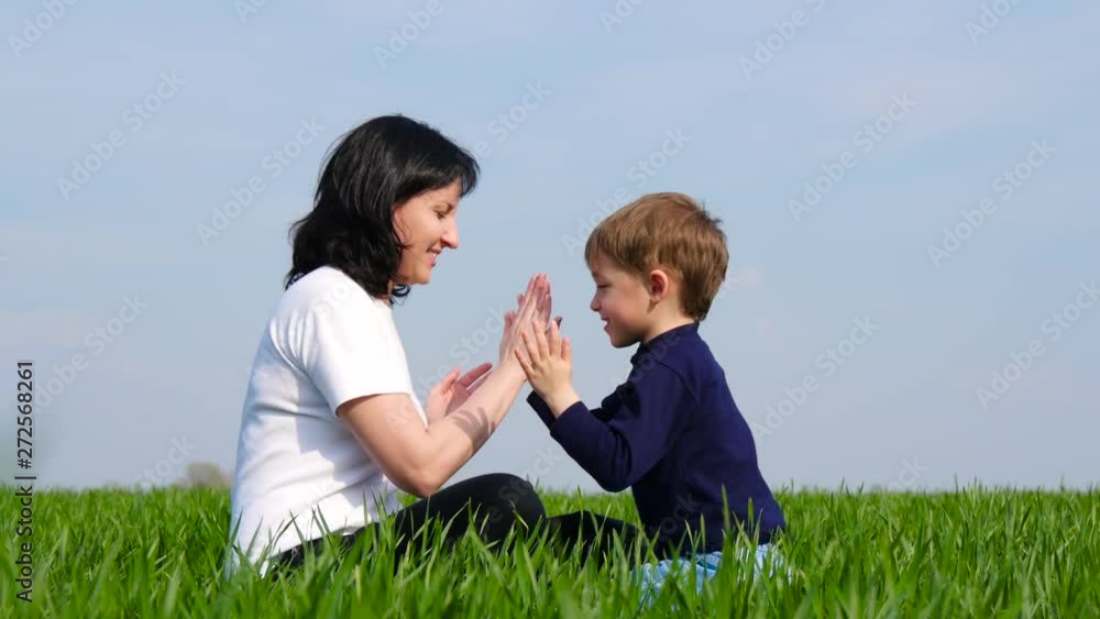 Happy family: mother and child sit on green grass and play, slapping each other on Batty Happy family: mother and child sit on green grass and play, slapping each other on Batty