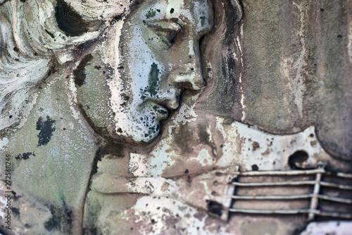 Partial view of a weathered metal relief of a violin playing woman on an old graveyard in Berlin-Germany.