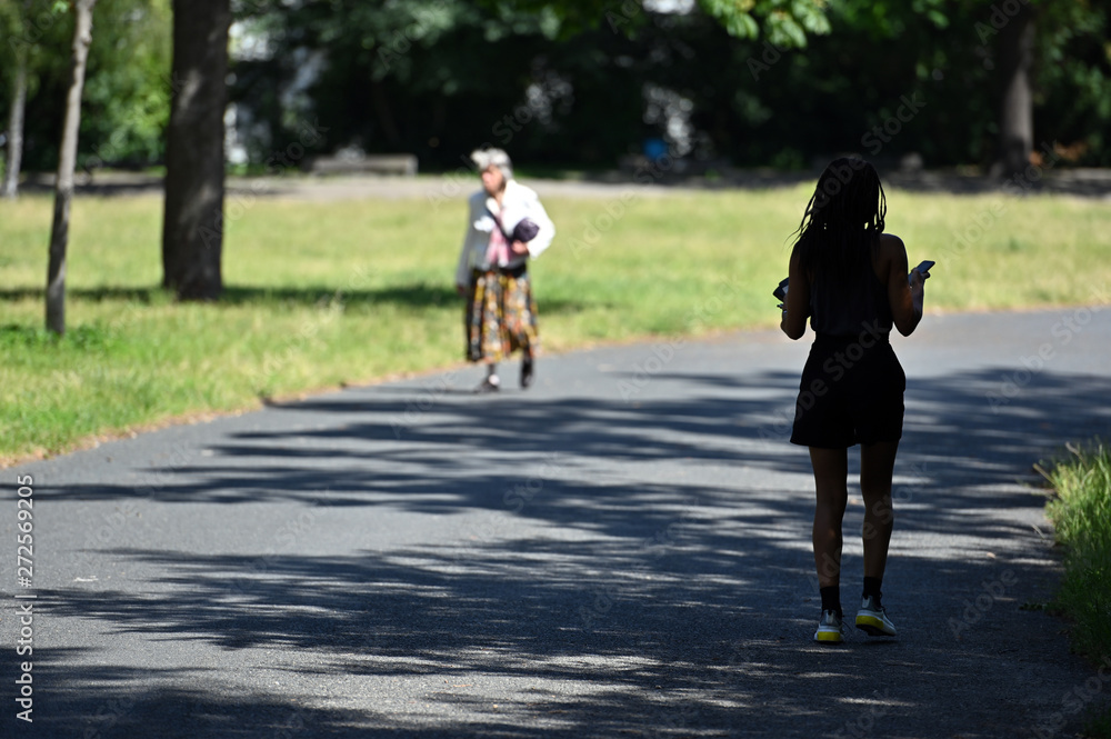 A young woman with ethnic background runs through a shadow of a tree in a berliner park on a warm summer day. An elderly woman comes to meet her.