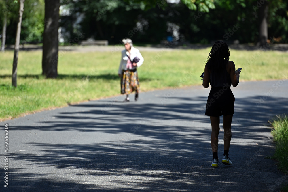 A young woman with ethnic background runs through a shadow of a tree in a berliner park on a warm summer day. An elderly woman comes to meet her. A young woman with ethnic background runs through a shadow of a tree in a berliner park on a warm summer day. An elderly woman comes to meet her.