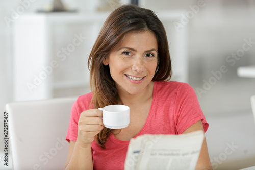 portrait of young woman drinking coffee and reading newspaper