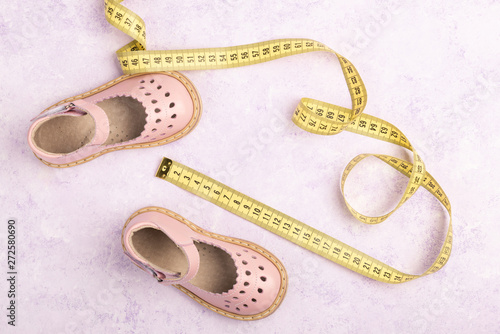 Summer Pink Baby girl shoes and Yellow measuring tape on violet marble background. Top view trendy leather sandal, flat lay. Copy space for your text