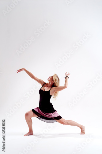 Photo of dancing slender blonde girl looking up in black dress in studio isolated