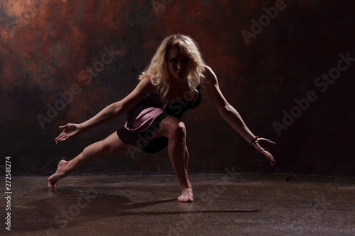 Full-length photo of dancing blonde girl in black dress on brown background