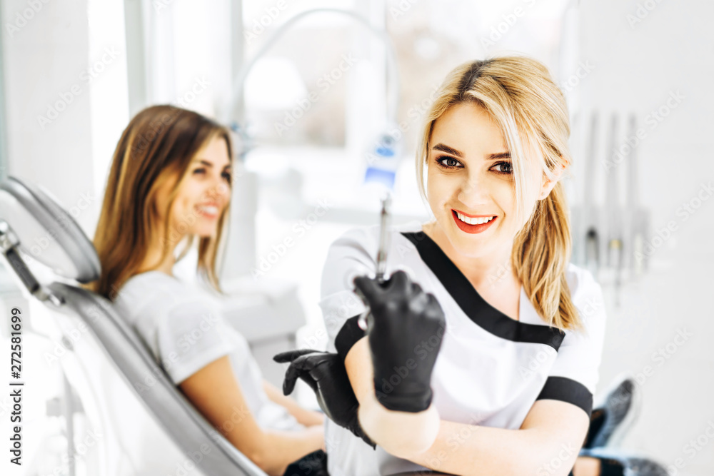 Pretty young dentist holding syringe with patient behind. Pretty young dentist holding syringe with patient behind.