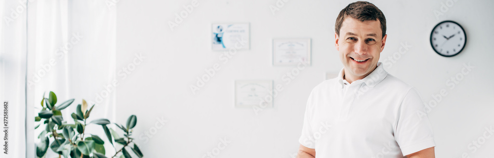 panoramic shot of smiling chiropractor in hospital looking at camera panoramic shot of smiling chiropractor in hospital looking at camera