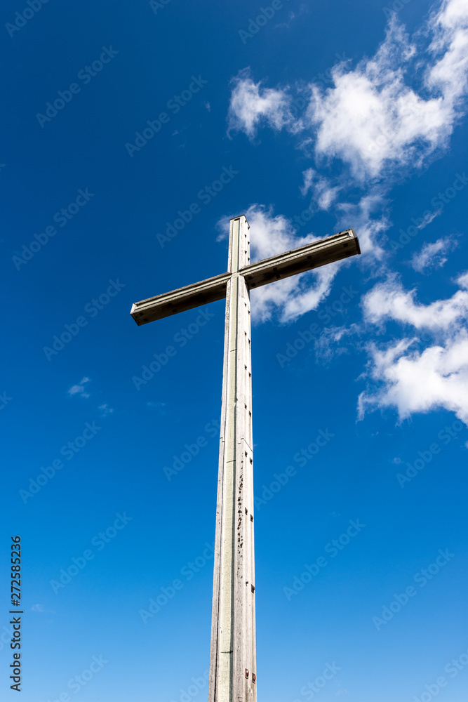 One wooden Christian cross on clear blue sky with clouds and copy space. Religious symbol in Italian Alps